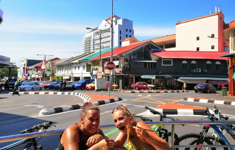 Guests pose with a bowl of noodles on a quick stop on their cycling Kuching day tour.