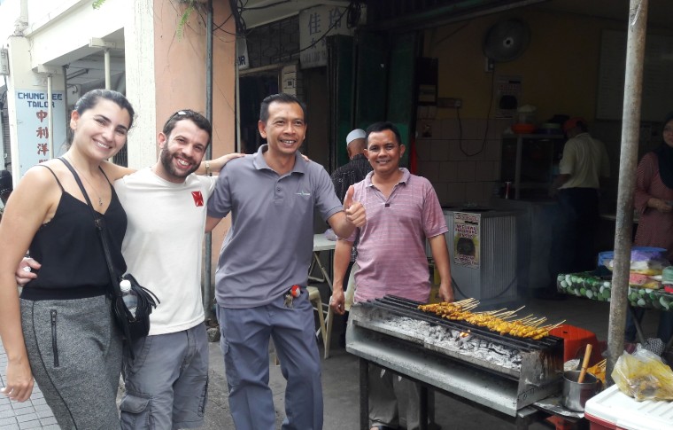 Guests pose for a photo next to kebabs cooking on the barbecue on this Kuching tour.