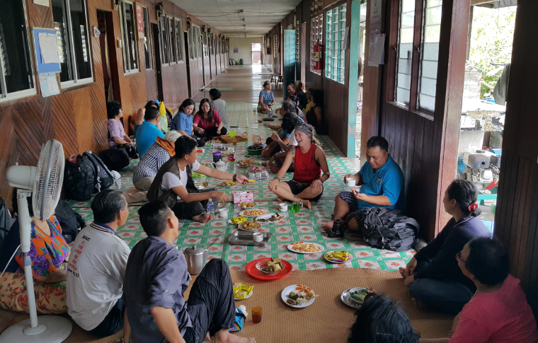 A group of people sit crosslegged on the floor to eat a meal.