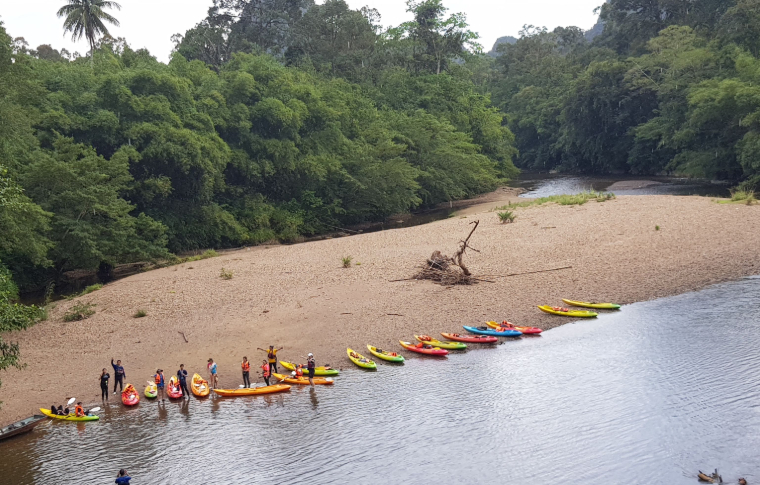 Kayaks line the shore of a river and guests hop into them to embark on their Borneo kayak adventure.