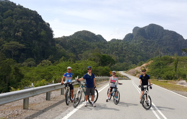Four people in cycling gear pose for the camera as they cycle on a road on this Borneo cycling tour.