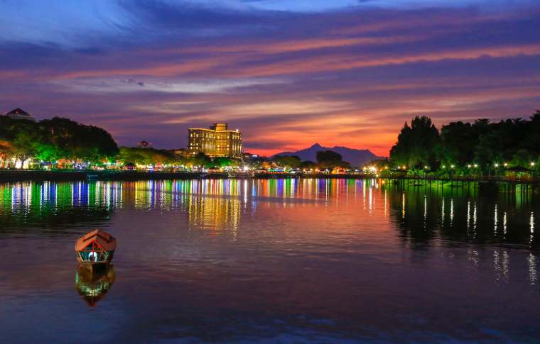 A city on the banks of a river is lit up at night on the best Borneo tours.