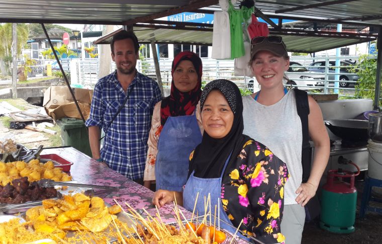 A couple stand next to two Bornean women as they make kebabs on a market stall on the Kuching day tour.