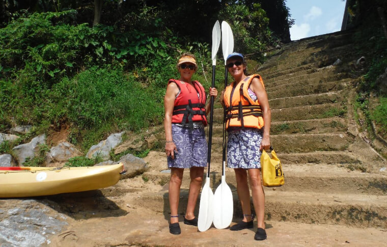 two women with paddles smiling at the bottom of stone stairs on a kayak adventure in Borneo