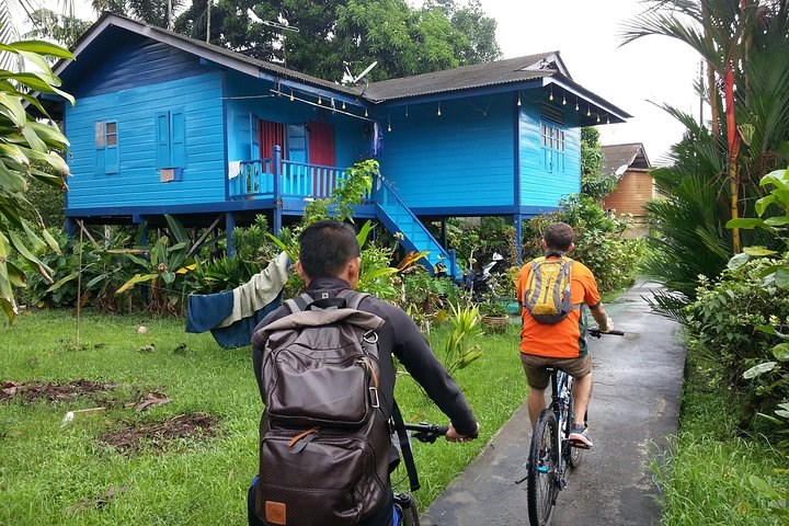 Two cyclists riding past blue kampung house